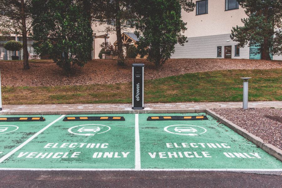 Parking avec deux places vertes réservées aux véhicules électriques, une borne et des arbres